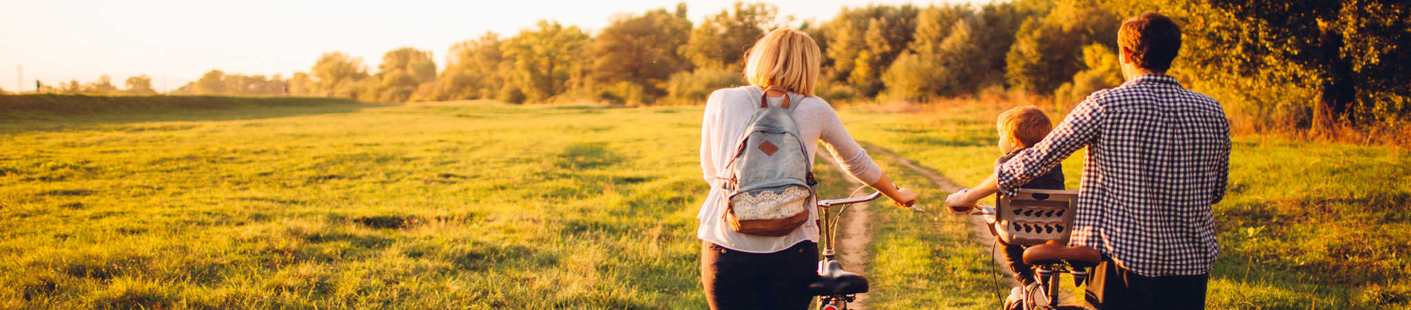 A father, mother, and child are walking through a sunny field with bicycles. This symbolizes estate planning.