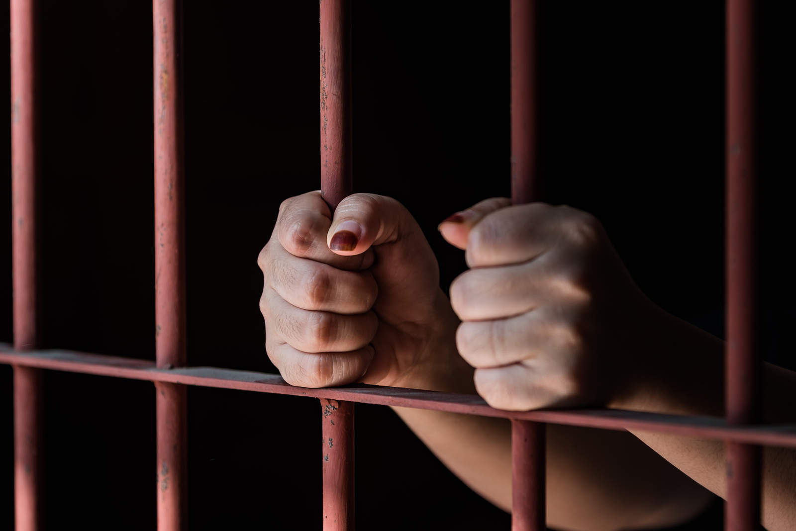 An individual in jail holds on to jail bars.