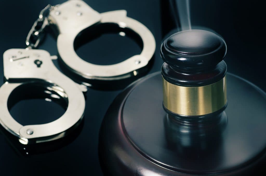 Handcuffs and a judge's gavel are sitting next to each other.