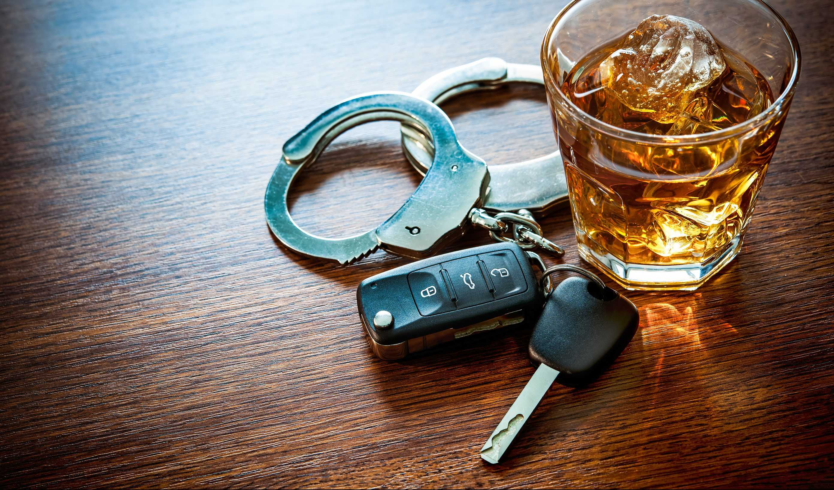 Handcuffs, a cocktail, and car keys sit on a table, symbolizing a DUI.