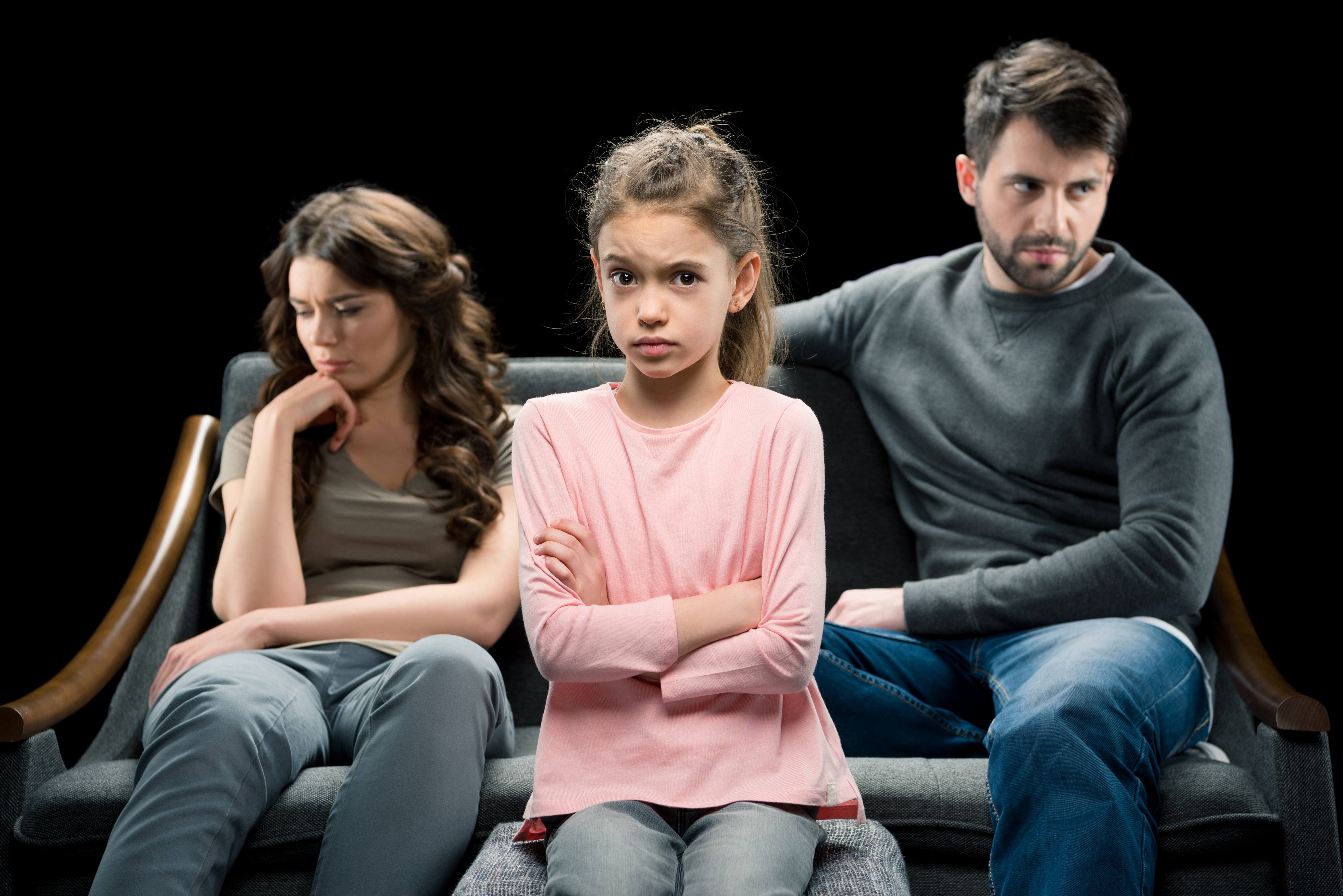 A distraught child sits between two parents who are divorcing.