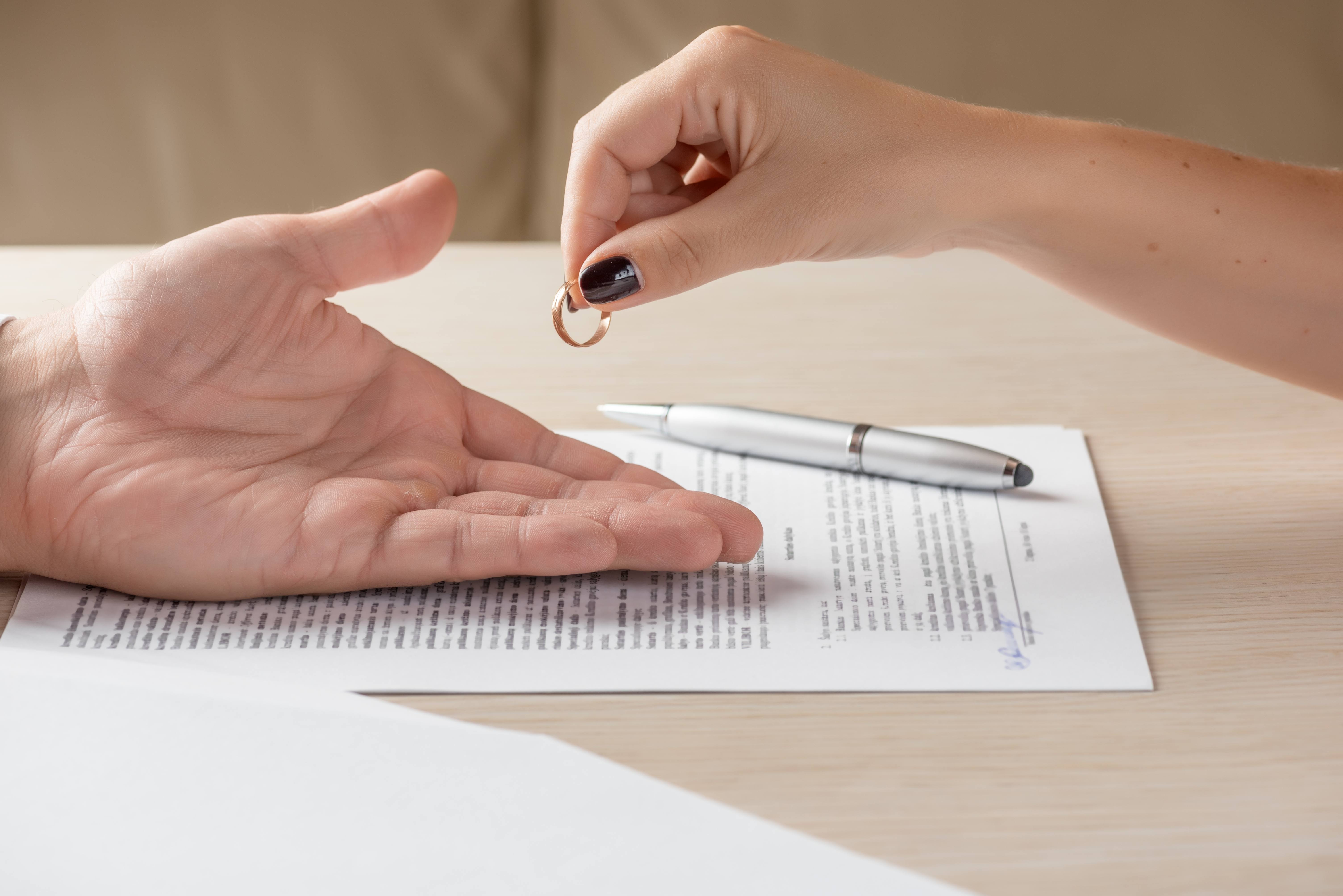 One spouse hands over their wedding ring to another spouse after signing divorce paperwork.