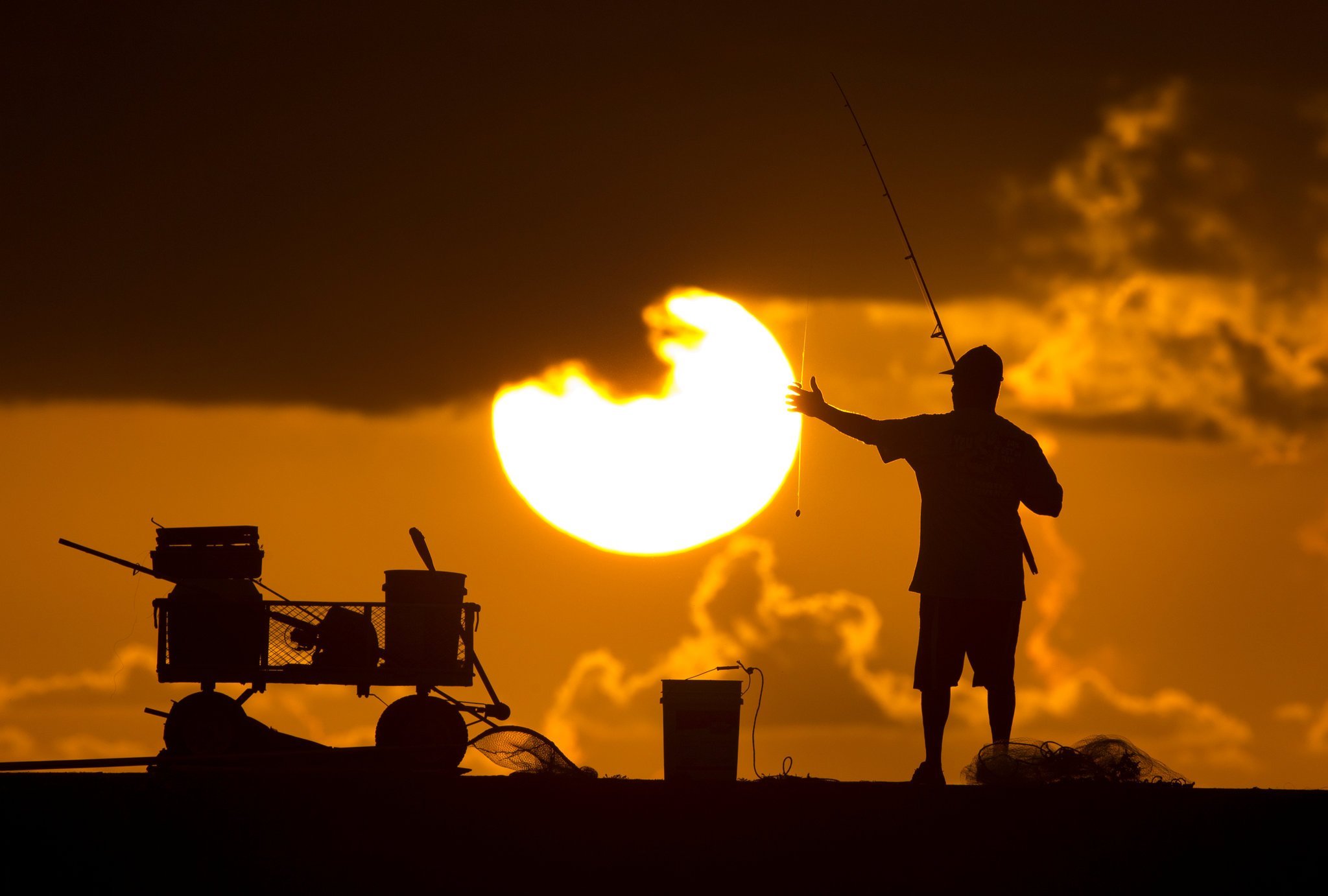 A silhouette of a person fishing during sunset.